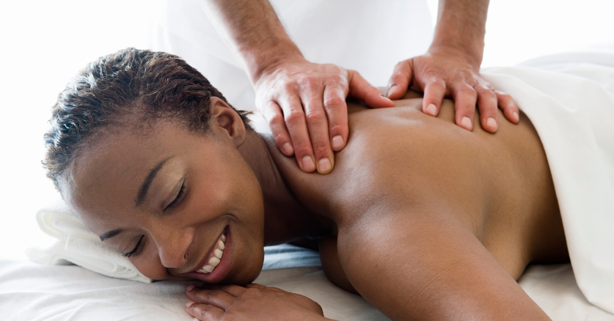 Woman receiving a relaxing back massage in a spa setting, smiling with eyes closed as the massage therapist works on her shoulders.