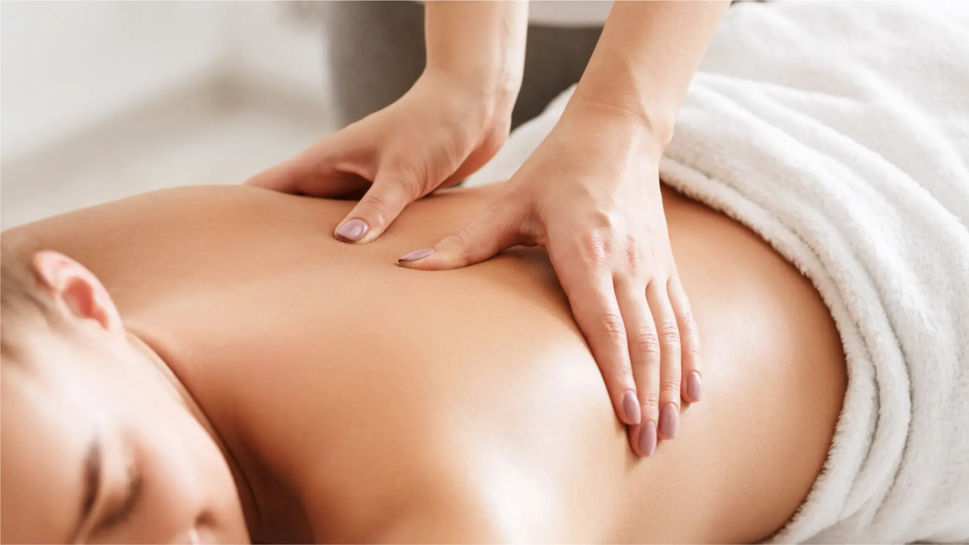 Woman receiving a relaxing back massage in a spa setting, smiling with eyes closed as the massage therapist works on her shoulders.