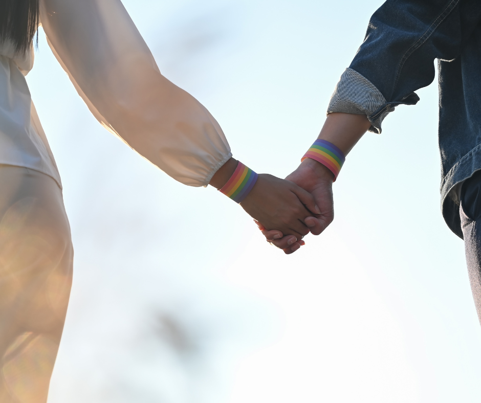 queer couple holding hands with rainbow bracelets