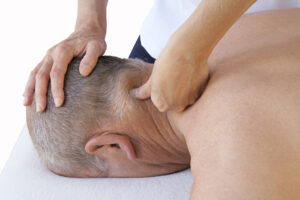 Massage therapist applying trigger point therapy to the neck of an older man lying face down, focusing on muscle tension relief.