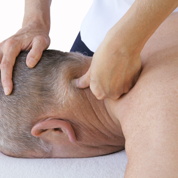 Massage therapist applying trigger point therapy to the neck of an older man lying face down, focusing on muscle tension relief.