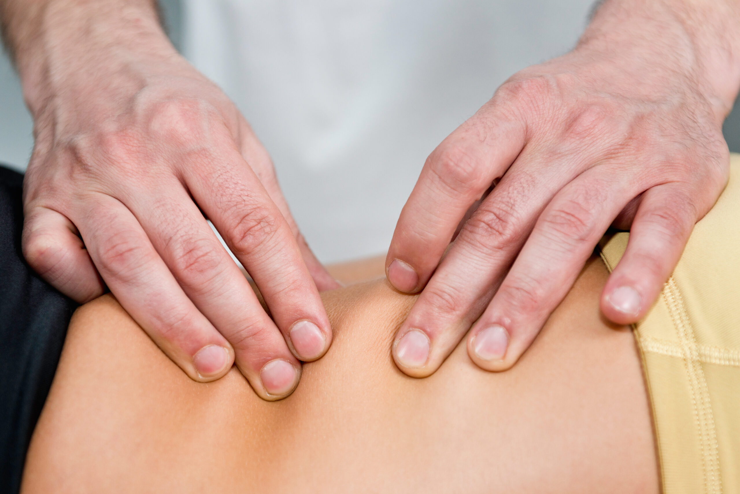 Close-up of therapist’s hands applying pressure along a client’s lower back during a myofascial release massage session