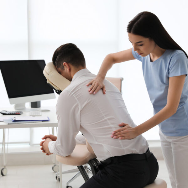 Female office worker receiving back massage in chair from female therapist in bright office