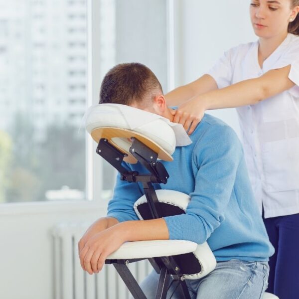 Male office worker receiving shoulder massage in chair at workplace