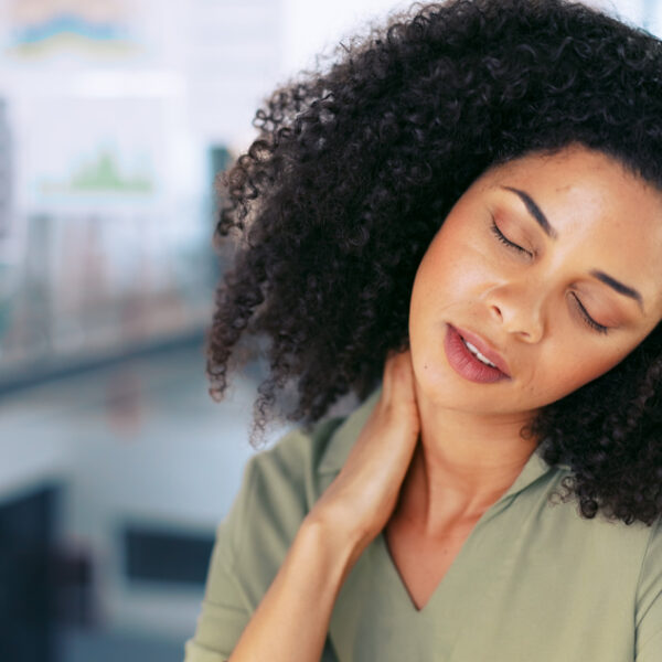 Office worker holding her neck in pain at desk, showing discomfort from workplace strain.