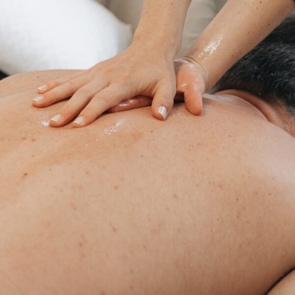 Therapist applying oil and performing a Swedish massage stroke across a client’s back in an at-home setting.
