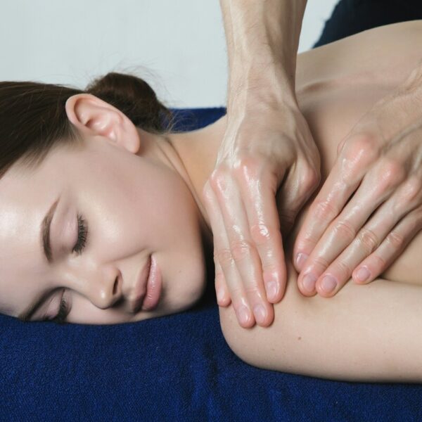 Close-up of a woman relaxing while receiving a Swedish massage with oil applied to her shoulder and upper arm.